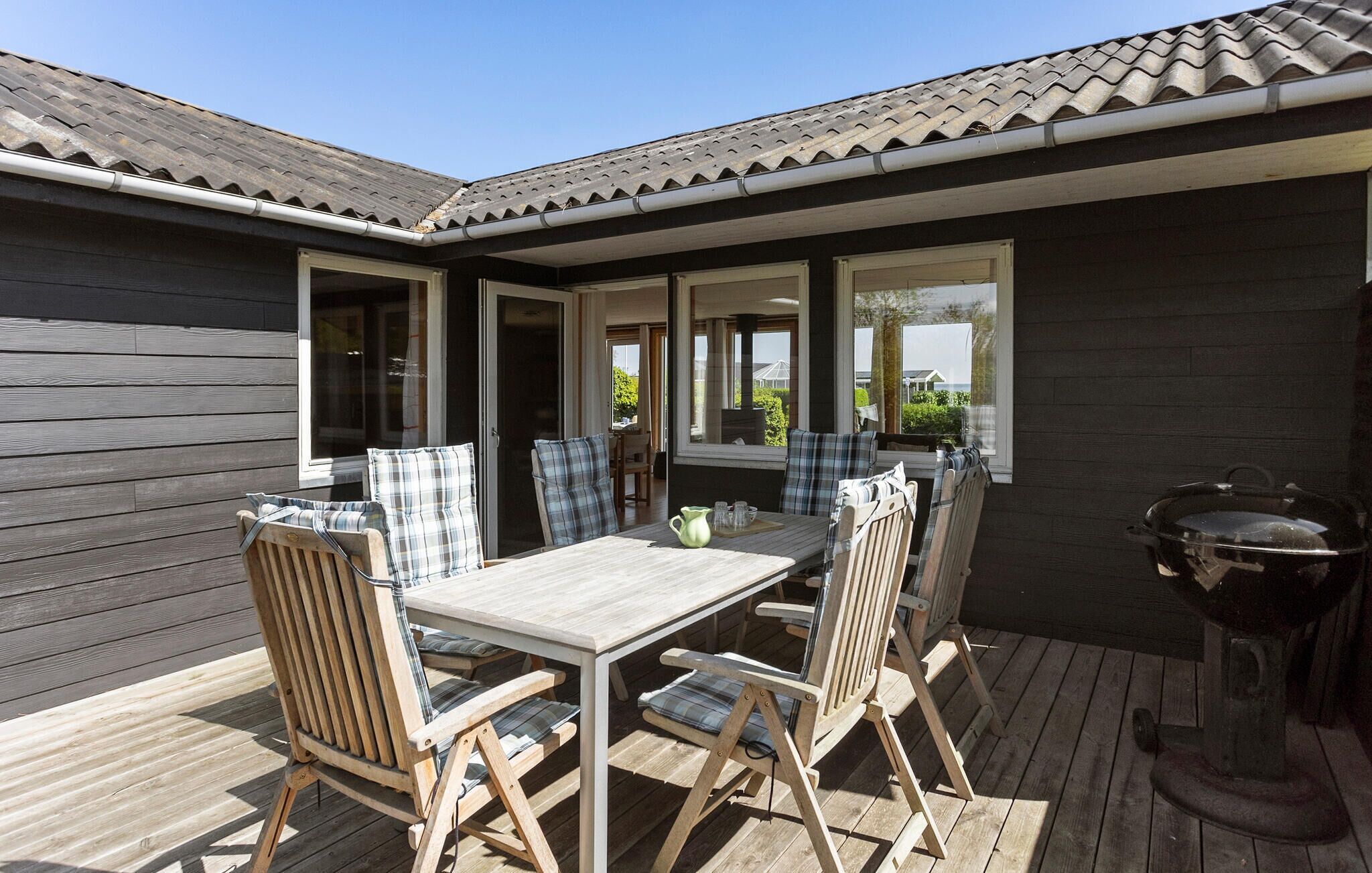 An outdoor patio with a wooden table and chairs, a grill, and large windows offering views of the surrounding area.