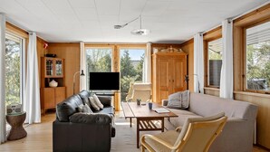A spacious living room with a leather sofa, a beige armchair, a wooden coffee table, and a television.