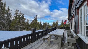A wooden deck with a table and benches, overlooking a forested area with a flag. - Nice home in Sjusjøen with WiFi (Sjusjøen)