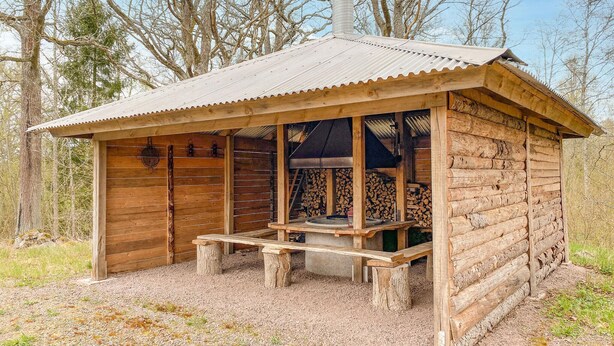 A rustic wooden cabin with a metal roof, a porch with benches, and a chimney. - 1 bedroom lovely home in Kättilstorp (Kättilstorp)