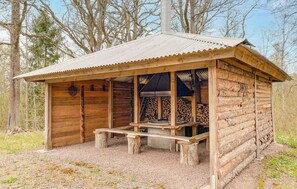 Una cabaña rústica de madera con techo metálico, un porche con bancos y una chimenea.