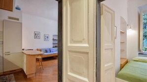 Ein gemütliches Zimmer mit einem hölzernen Schreibtisch, einem blau gestreiften Sofa und einem Bett mit grüner Bettdecke.