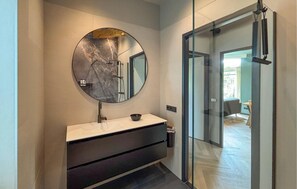 Un baño moderno con lavamanos de mármol, un espejo redondo y cabina de ducha de cristal.
