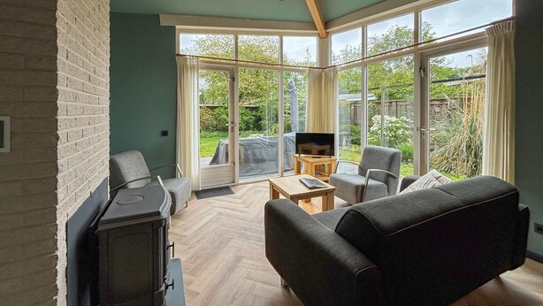 Ein modernes Wohnzimmer mit Kamin, einer Couch, einem Couchtisch und großen Fenstern mit Blick auf den Garten.