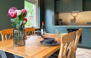 A dining area with a wooden table, chairs, a vase with flowers, a wine bottle, and a deer silhouette on the wall. - Cozy home in Putten with WiFi (Putten)
