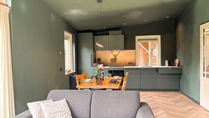 Ein modernes Wohnzimmer mit grauem Sofa, einem Esstisch mit Stühlen und einer Küche mit grauen Schränken und einem Fenster.