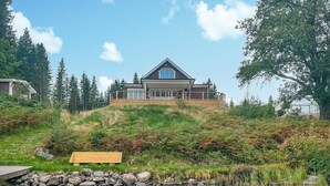 Ett modernt hus med en stor terrass, omgivet av en vacker natur och en vattenyta.