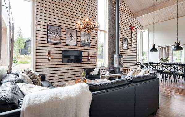 A modern living room with a large black sofa, wooden panel walls, a fireplace, and a dining area with a table and chairs.