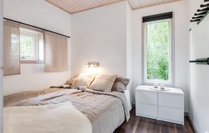 Relax in a serene space with a comfortable bed, bedside table, and large window offering a view of lush greenery.