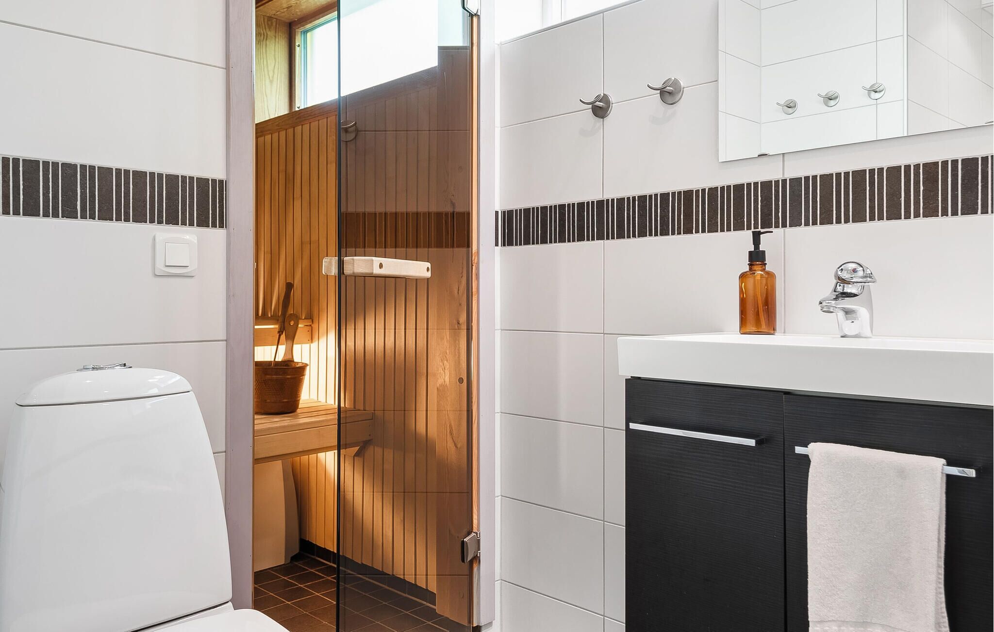 A modern bathroom with a glass-enclosed shower, a white toilet, a black cabinet, and a white sink with a towel hanging on the side.