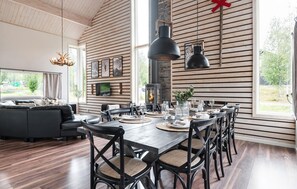 Relax in this elegantly designed living area with a high ceiling and exposed beams, featuring a large dining table and comfortable seating.