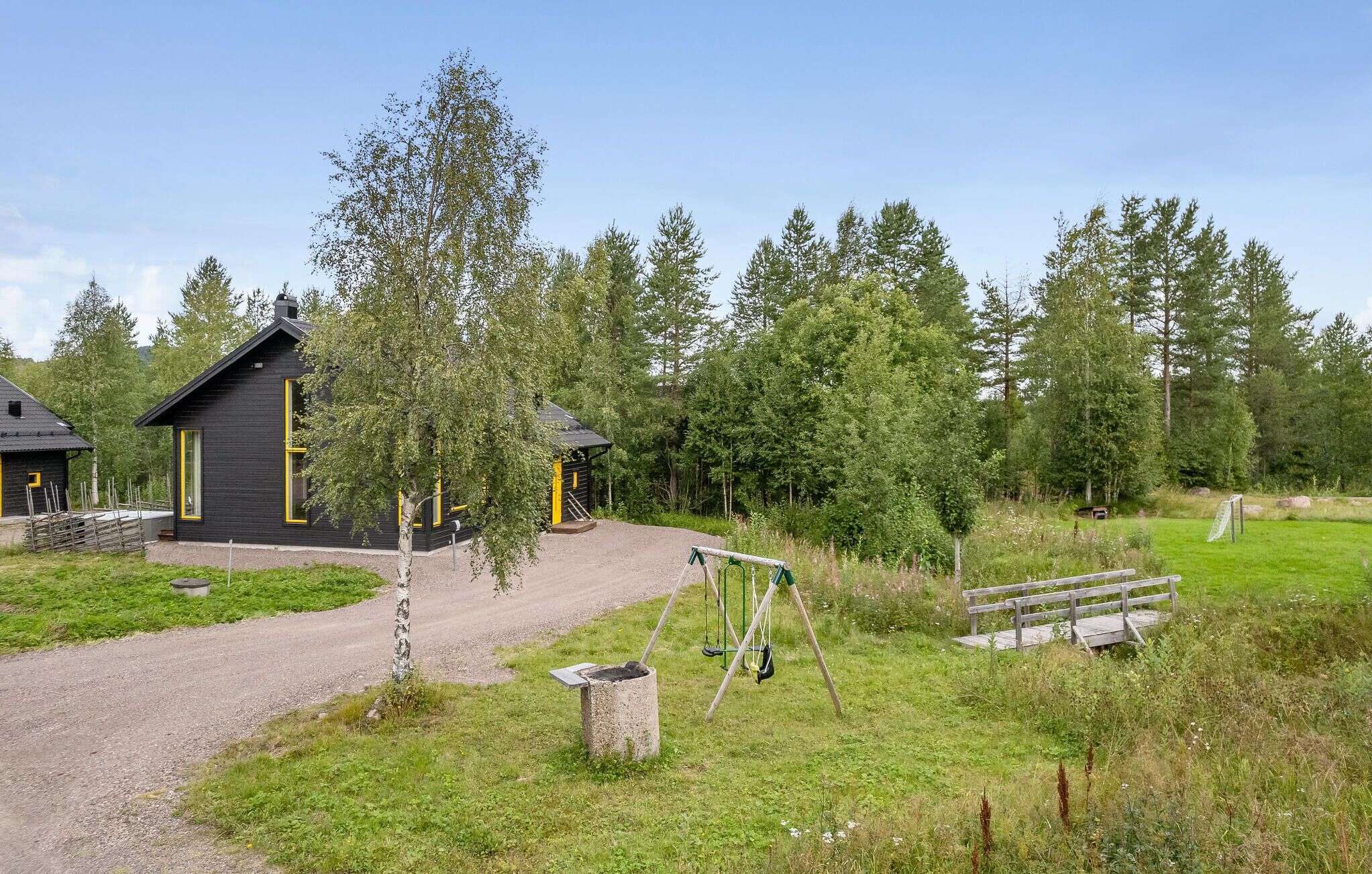 En rustik hytte med en grusvej, omgivet af frodigt grønt og træer.