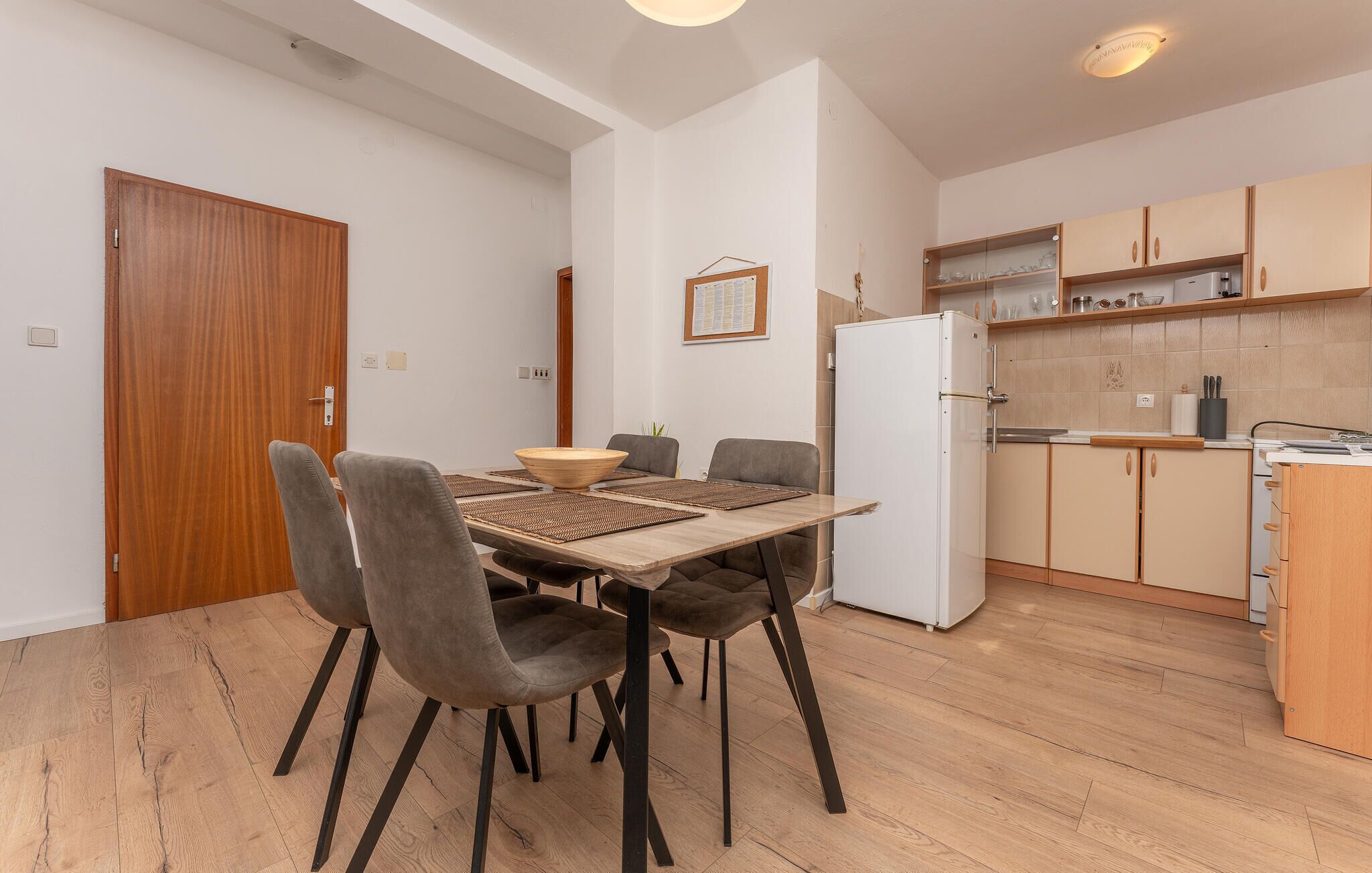 A modern kitchen with wooden cabinets, a white refrigerator, and a dining area with a table and chairs.