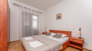 A bedroom with a wooden bed, two bedside tables with lamps, a window with sheer curtains, and a painting on the wall. - Awesome apartment in Biograd na Moru with WiFi (Biograd na Moru)