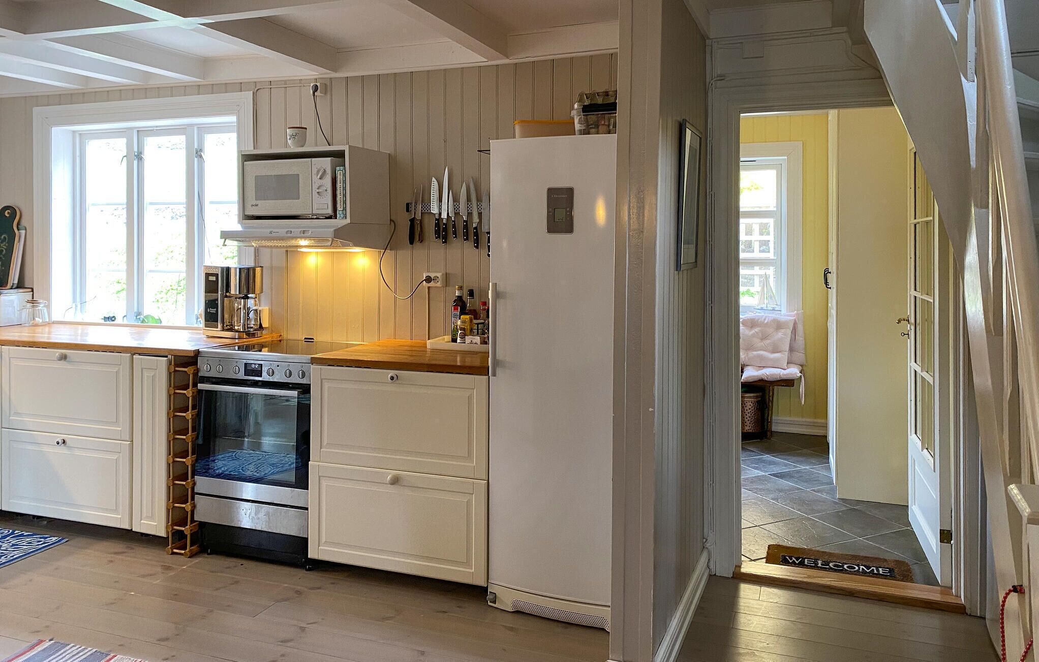 A compact kitchen with a stove, oven, microwave, and refrigerator. There is a wooden countertop and a ladder for accessing the upper cabinets.