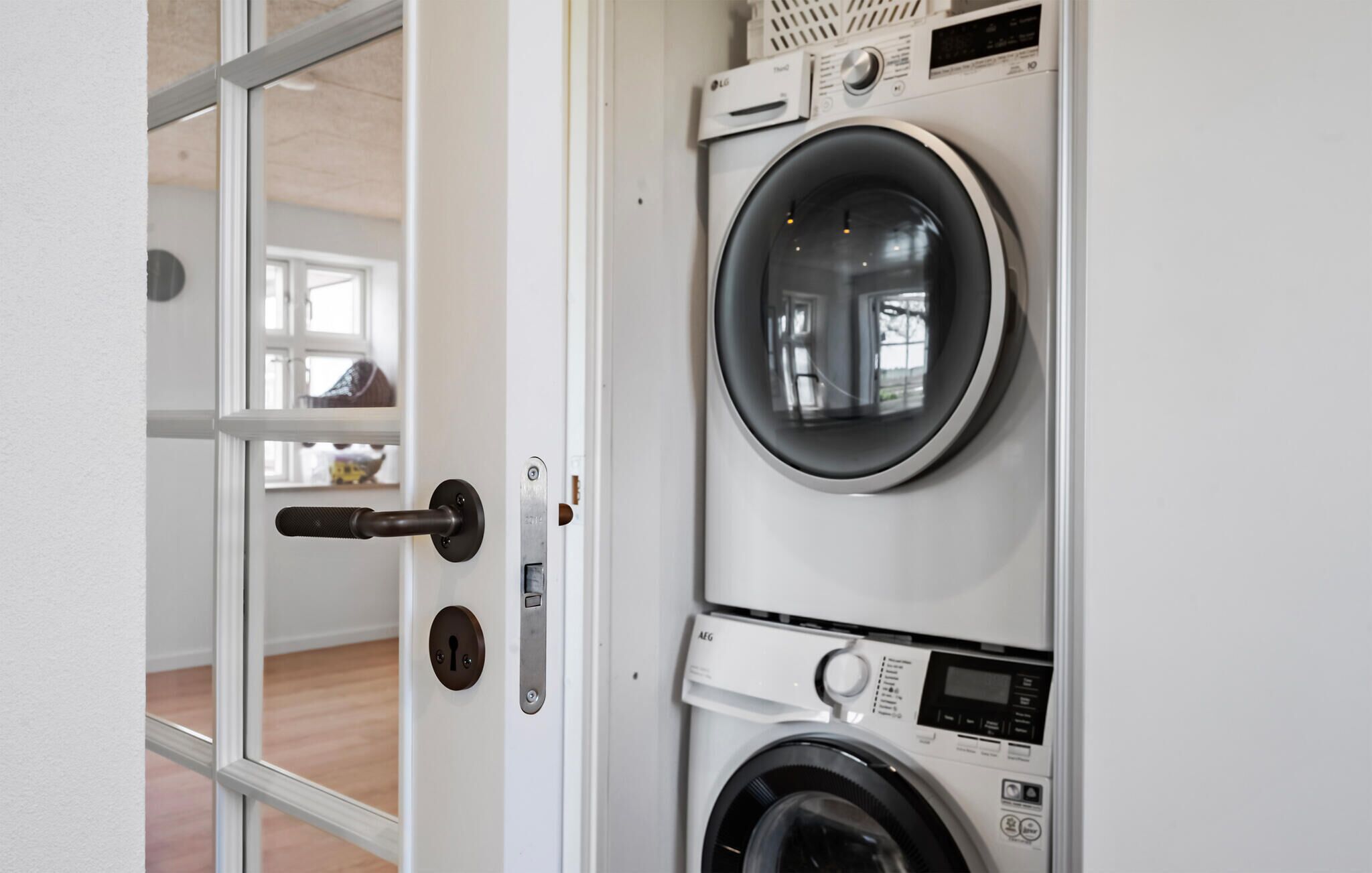 Een wasserette met een voorlader wasmachine en droger, een deur met sleutelslot, en een raam met uitzicht op het interieur.