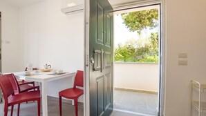 A dining area with a white table and red chairs, a door with a handle, and a view of greenery outside. - 2 bedroom beautiful home in Castellabate (Castellabate)