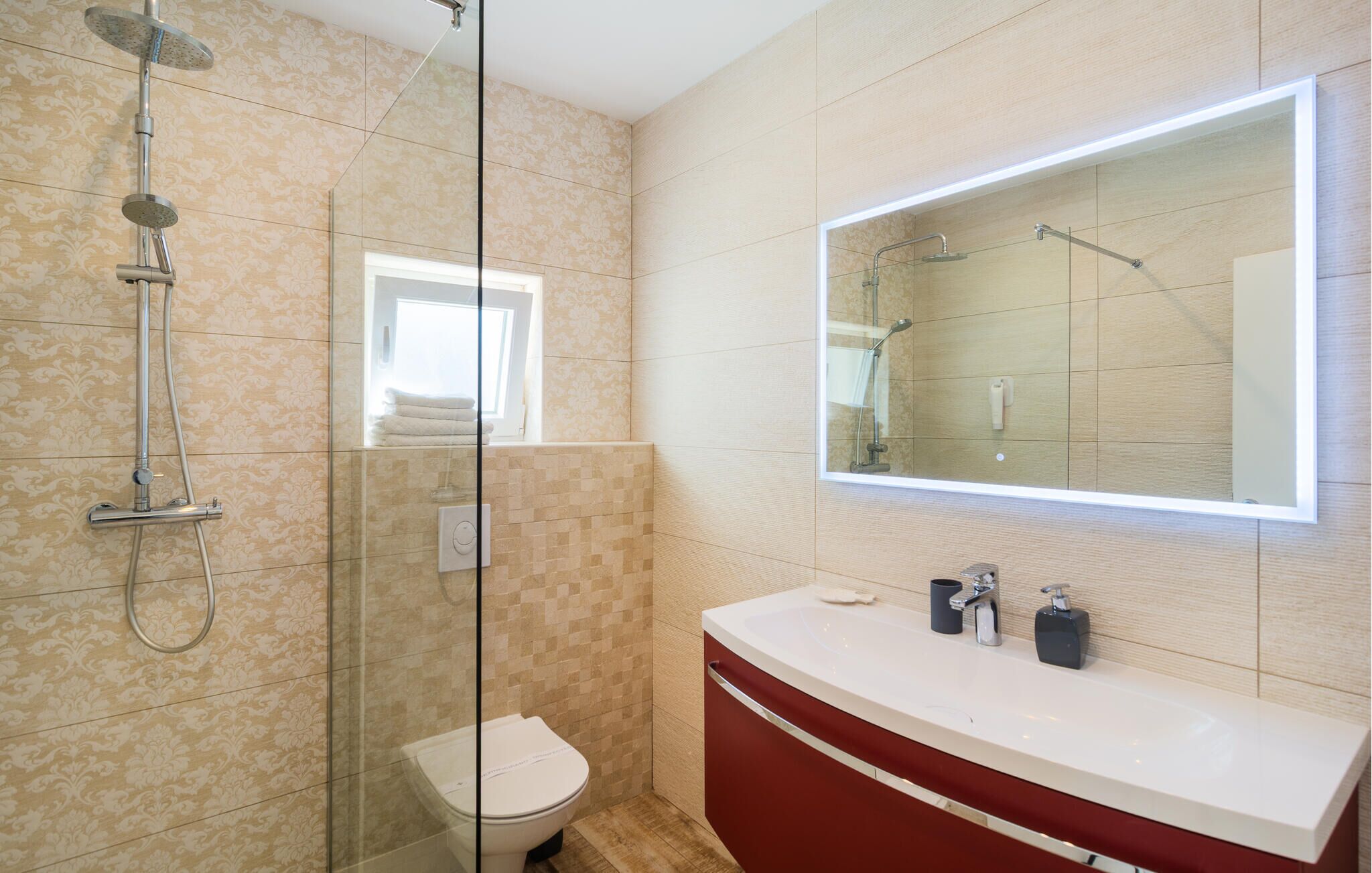 Een moderne badkamer met een douche met glazen wand, een toilet, een wastafel met spiegel en een raam.