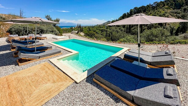 A pool area with lounge chairs and umbrellas, surrounded by a pebble beach and greenery. - Amazing home in Xylokastro with house a mountain view (Xylokastro)
