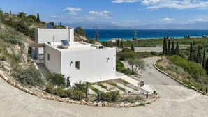 A modern white building with solar panels, surrounded by a landscaped garden and overlooking a coastal area with mountains in the background. - Amazing home in Xylokastro with house a mountain view (Xylokastro)