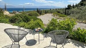 An outdoor seating area with two metal chairs and a small table, overlooking a scenic coastal landscape with mountains in the distance. - Amazing home in Xylokastro with house a mountain view (Xylokastro)