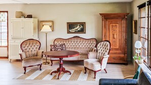 Una habitación con una mesa redonda de madera, dos sillones tapizados, un sofá, un aparador y un armario grande de madera.