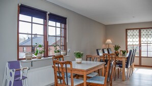 Un comedor con una mesa y sillas de madera, plantas en macetas y vistas al exterior a través de ventanas amplias.