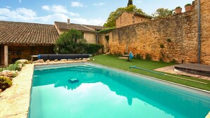 A swimming pool with a stone wall and a tiled roof structure in the background. - Stunning home in Sabran with heated swimming pool (Sabran)