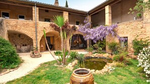 A courtyard with a stone building, a small pond, and purple flowering plants. - Stunning home in Sabran with heated swimming pool (Sabran)