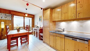 A kitchen with wooden cabinets, a sink, and a dining area with a table and chairs. - Gorgeous apartment in Gérardmer with WiFi (Gérardmer)