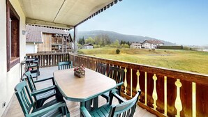 A balcony with a wooden table and chairs, overlooking a rural landscape with houses and mountains. - Gorgeous apartment in Gérardmer with WiFi (Gérardmer)