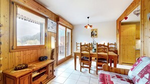 A cozy room with wooden walls and a large window, a dining table with chairs, and a sofa with a patterned cover. - Gorgeous apartment in Gérardmer with WiFi (Gérardmer)