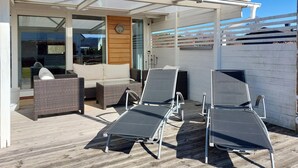 A covered outdoor seating area with two lounge chairs and a table, a wooden deck, and a glass door leading inside. - 4 bedroom nice home in Båstad (Båstad)