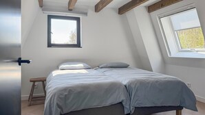 A bedroom with a bed, a window, and a wooden beam ceiling.