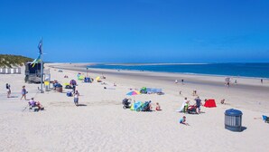 A beach with people sunbathing and walking, a lifeguard tower, and a clear blue sky.