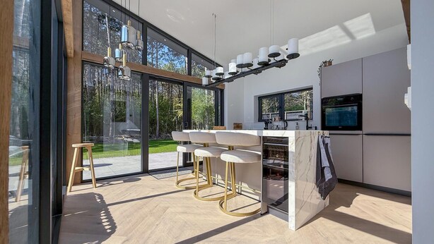 A modern kitchen with a bar area, large windows, and a view of the outdoors.