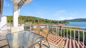 A balcony with a glass table and chairs, overlooking a lake and hills. - Stunning apartment in Pirovac with WiFi (Pirovac)