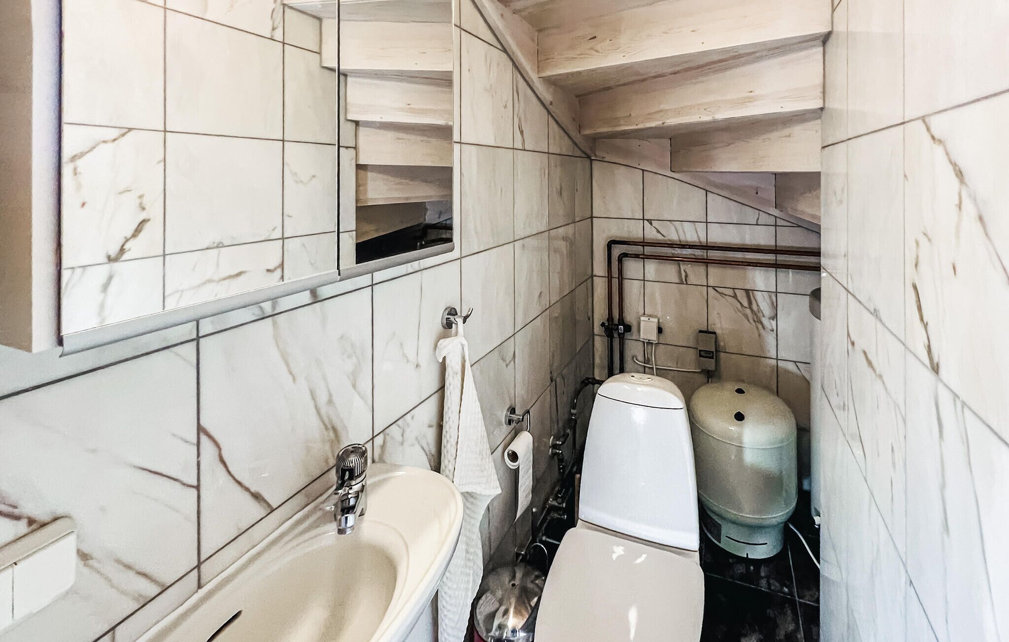 Une salle de bain avec un mur recouvert de carreaux de marbre, un lavabo, des toilettes et un distributeur d’eau.