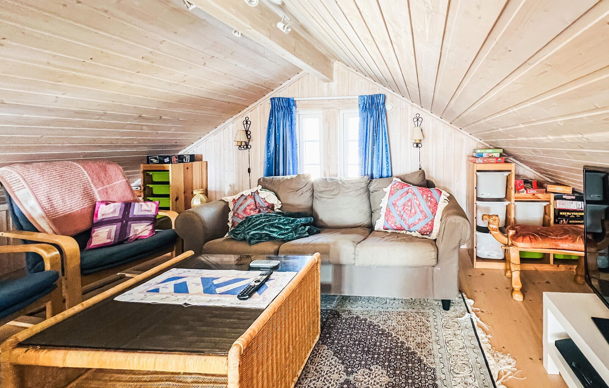A cozy attic room with a sofa, a chair, a small table, and a bookshelf.