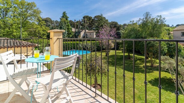 Un balcon avec une table et des chaises, une piscine et un jardin bien entretenu.