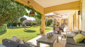 Une terrasse extérieure aménagée avec un canapé, une table et des chaises, entourée de verdure et agrémentée d’une pergola.