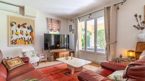 Un salon avec un téléviseur, des canapés en cuir, une table basse et une grande fenêtre avec des rideaux.