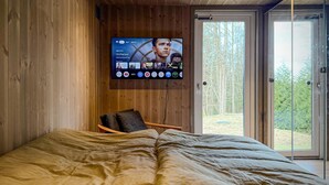 A bedroom with a large bed, a wooden wall, a TV mounted above it, and a door leading to a forested area. - Cozy home in Tollered with WiFi (Tollered)