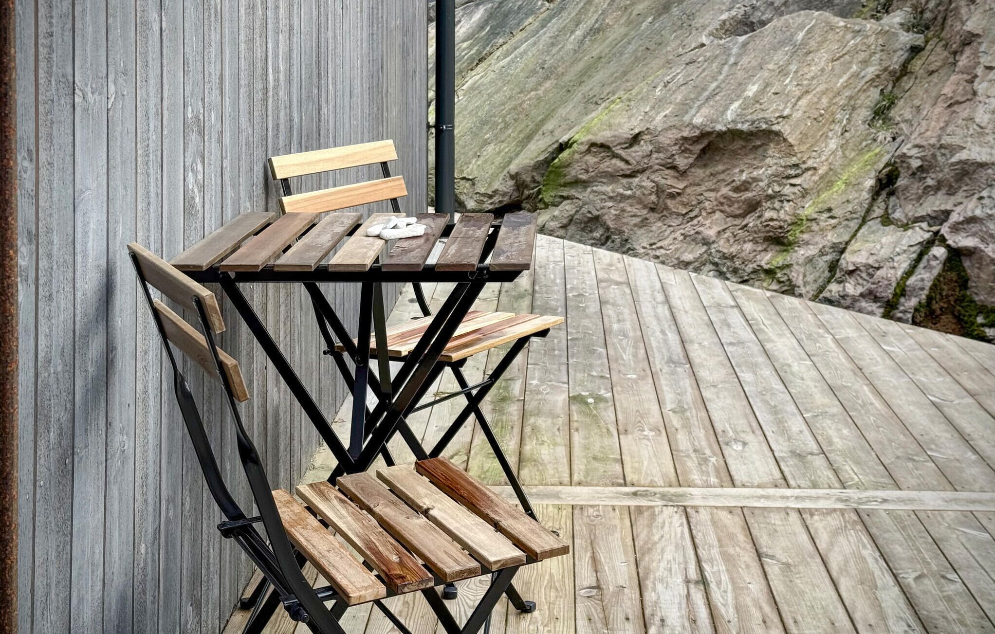 Mesa de madeira com bancos encostada a uma parede, sobre um deck de madeira com paisagem rochosa ao fundo.