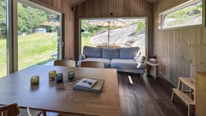 A cozy cabin interior with a wooden table, a sofa, and a view of a rocky outdoor area. - Cozy home in Tollered with WiFi (Tollered)
