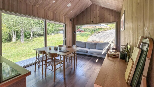 A modern interior with a wooden ceiling, a dining area with a table and chairs, a sofa, and a large window offering a view of a grassy area and trees. - Cozy home in Tollered with WiFi (Tollered)