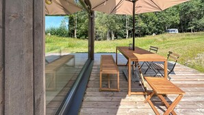 An outdoor wooden deck with a table and benches, a glass enclosure, and a large umbrella providing shade. - Cozy home in Tollered with WiFi (Tollered)