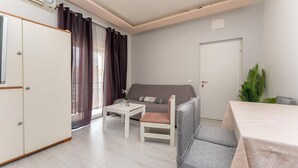 Una habitación pequeña con un sofá gris, una mesita, un armario blanco y una puerta.