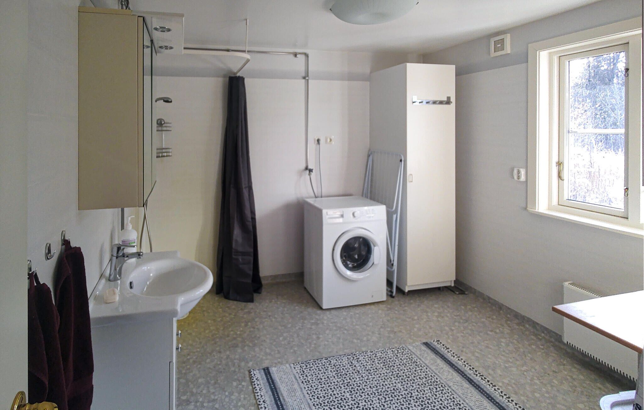 A compact bathroom with a sink, mirror, towel rack, washing machine, and a window.