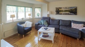 Ein Wohnzimmer mit grauem Sofa, einem weißen Couchtisch mit Büchern, einem blauen Sessel und einem Bild an der Wand.